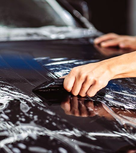 a hand sweeping water out from under a car wrap